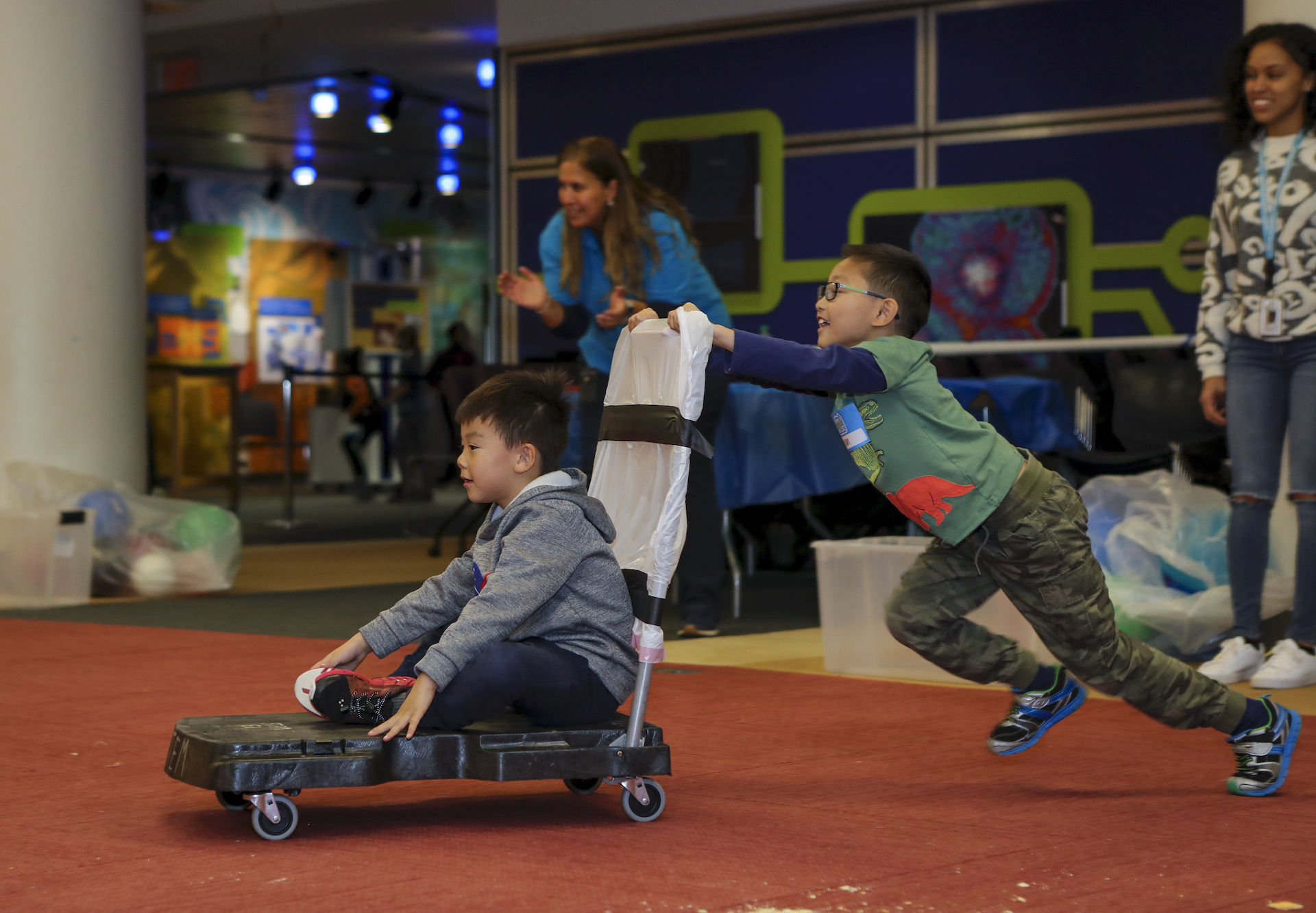 Kids playing a game where one of them is pushed on a cart