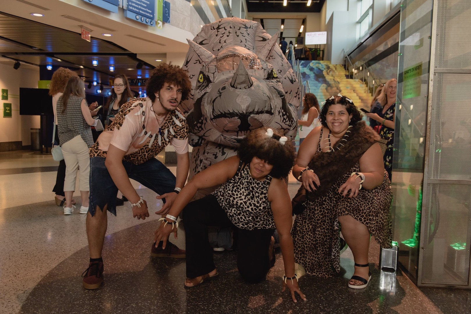 Three guests in cavemen costumes pose with a dinosaur costume character